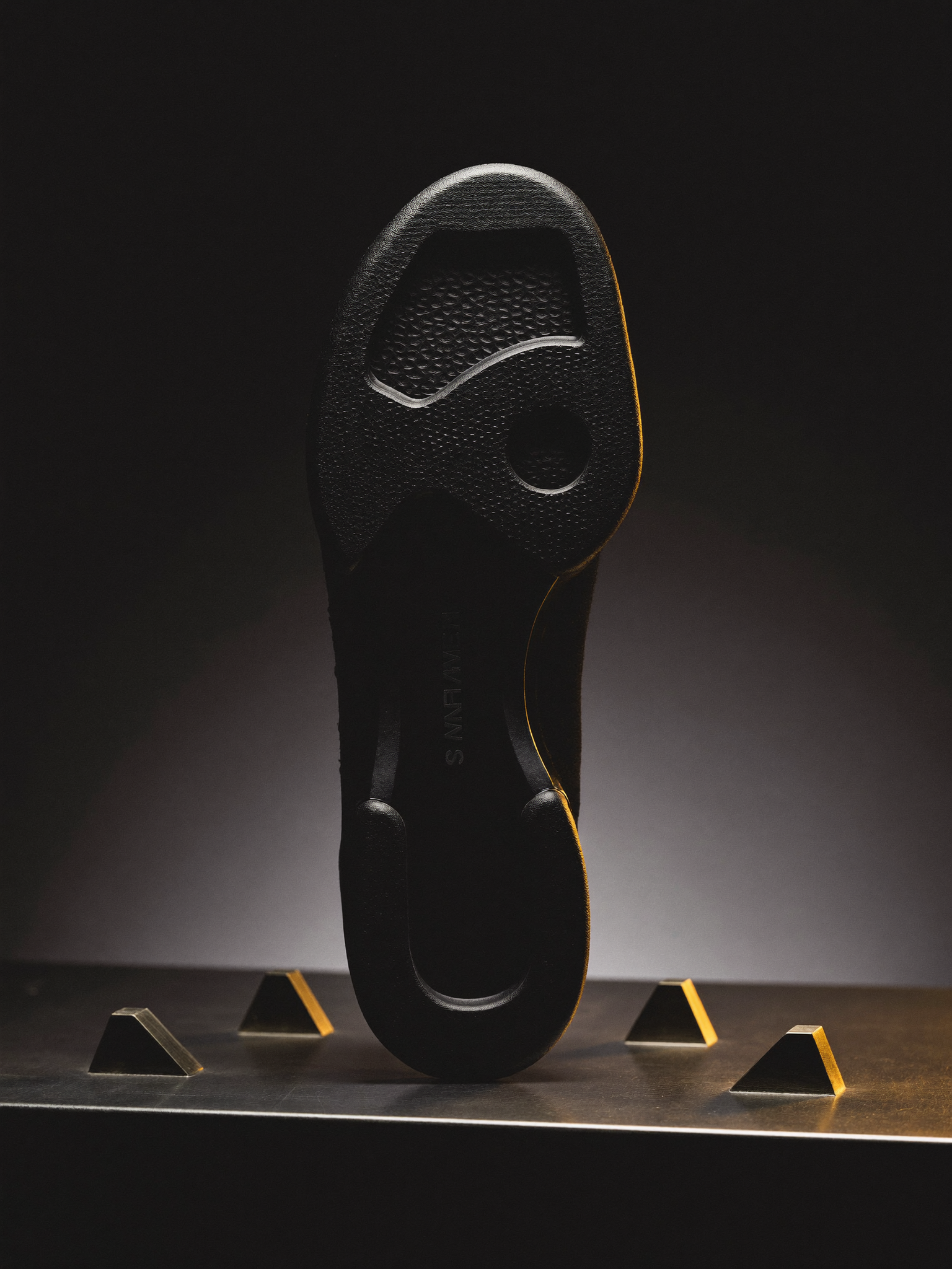 Die Sohle eines Sneakers wird auf einer dunklen Metallwerkbank im Streiflicht begutachtet