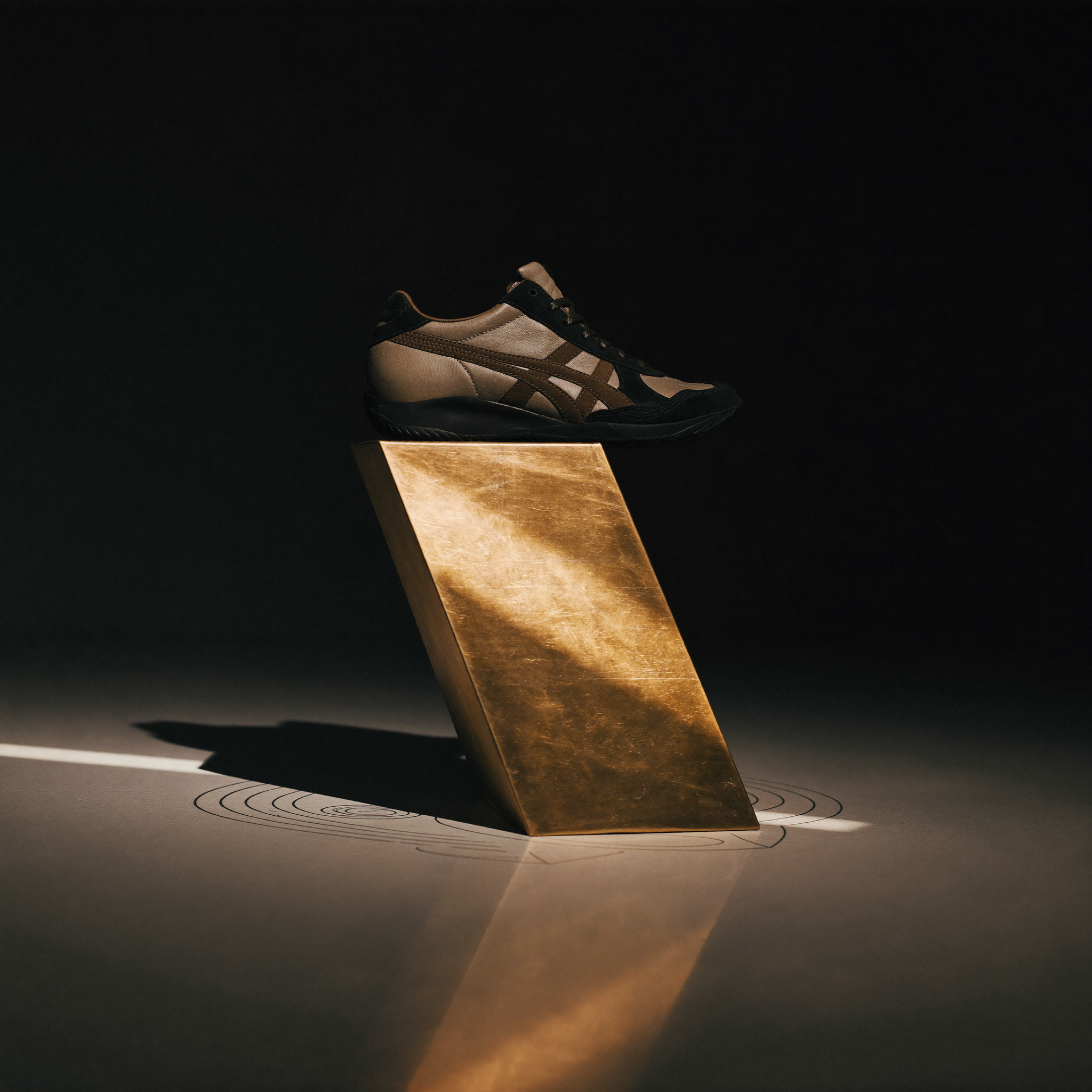 Ein einzelner Sneaker auf einer dunklen Messingplinthe, allein im fast leeren Studio, mit langem dramatischen Schatten